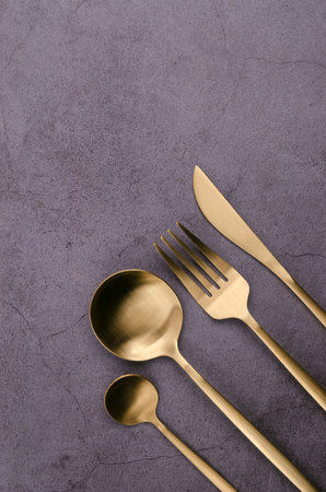 Clean golden metal cutlery on a dark background. design concept. top view.
