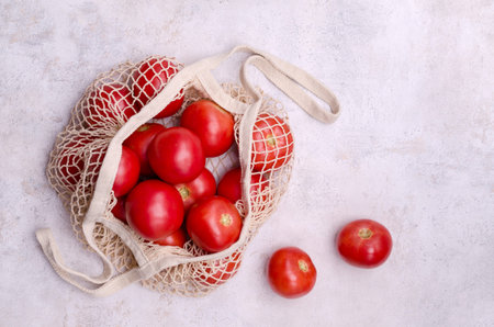 Large raw red tomatoes in a mesh bag on a light background. Eco friend concept. top view.