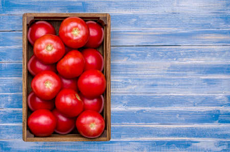 Large raw red tomatoes in a wooden box on a blue background. Eco friend concept. top view.の写真素材