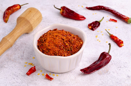 Red dry pepper powder and slices in a ceramic dish on a light background. selective focus.