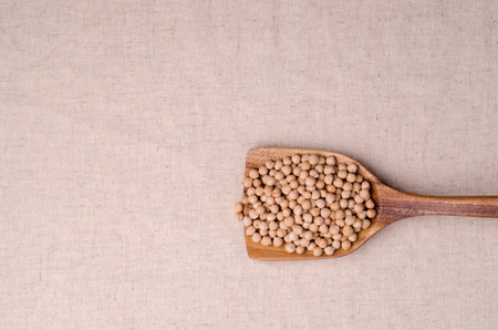Dry organic chickpeas in a wooden scoop on a textile background. top view.の写真素材