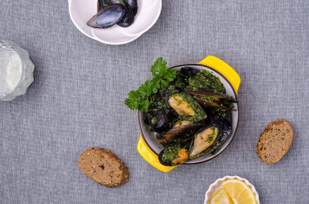 Mussels with green sauce in a dish on a textile background. top view.
