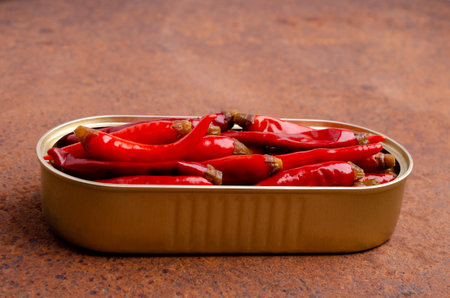 Pickled red hot peppers in a tin can on a rusty metal background. selective focus.