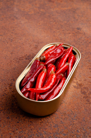 Pickled red hot peppers in a tin can on a rusty metal background. selective focus.の写真素材