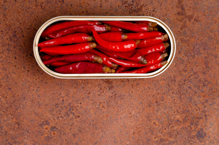 Pickled red hot peppers in a tin can on a rusty metal background. top view.