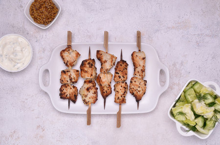 Fried slices of meat on wooden skewers. Raw vegetable salad, mustard and sour cream. view from...