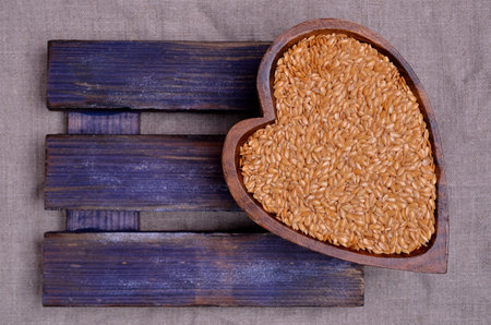 Yellow flax seeds in a wooden dish on a textile background. Top view.の写真素材