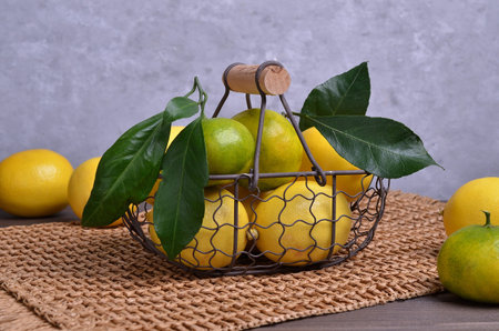 Ripe citrus fruits with leaves in a metal basket on a dark wooden background. Selective focus.
