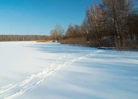 footprints in the snow, a frozen snow-capped lake and a blue skyの写真素材