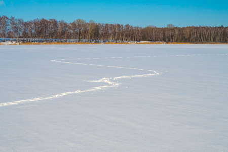 footprints in the snow, a frozen snow-capped lake and a blue skyの写真素材