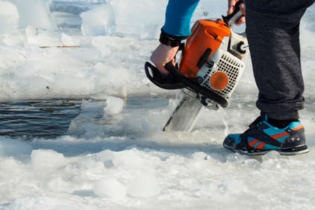 a man with a chainsaw cuts the ice on the lakeの写真素材