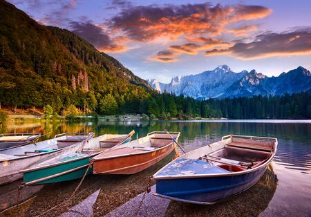 Amazing view on Lago di Fusine Inferiore at sunrise. Splendid morning scene of Julian Alps, Province of Udine, Italy, Europe. Beautiful forests are reflected in the quiet lake. Four pleasure boatsの写真素材