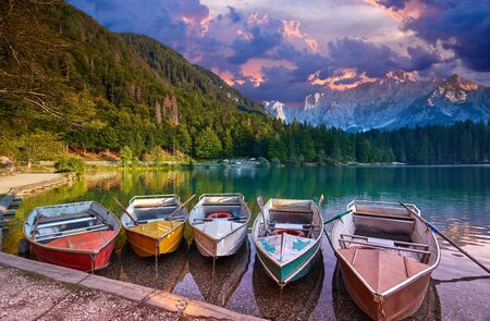 Amazing view on Lago di Fusine Inferiore at sunrise. Splendid morning scene of Julian Alps, Province of Udine, Italy, Europe. Beautiful forests are reflected in the quiet lake. Four pleasure boatsの写真素材