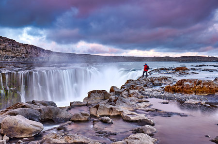 Photographer hiker with a travel backpack and tripod near Selfoss waterfall. Iceland, Jokulsa...