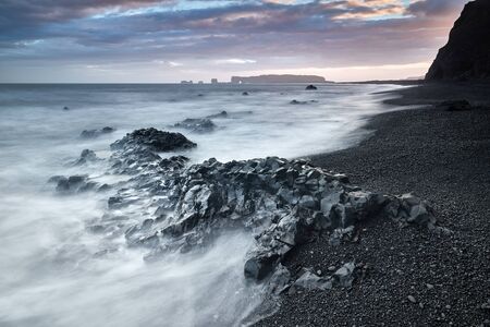 View on Dyrholaey Lighthouse. Famous tourist landscape with basalt rock formations Troll toes on black beach. Ocean waves flow around stones. Reynisdrangar, Vik, Iceland, Atlantic Ocean, Europe.の写真素材