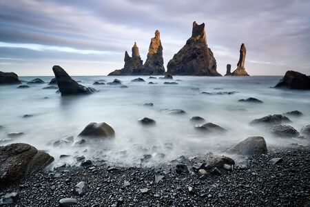 Famous tourist landscape with basalt rock formations Troll toes (Trolls fingers) on black beach. Ocean waves flow around stones. Reynisdrangar, Vik, Iceland, Atlantic Ocean, Europe. Travel postcard.の写真素材