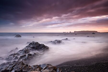 View on Dyrholaey Lighthouse. Famous tourist landscape with basalt rock formations Troll toes on black beach. Ocean waves flow around stones. Reynisdrangar, Vik, Iceland, Atlantic Ocean, Europe.の写真素材