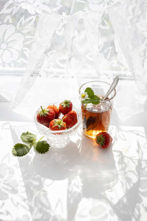 Cup of tea and wild strawberries on a white lace backgroundの写真素材