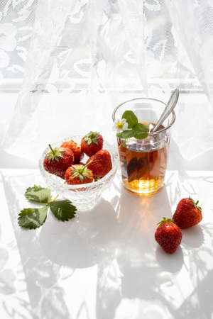 Cup of tea and wild strawberries on a white lace backgroundの写真素材