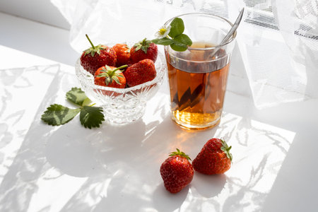 Cup of tea and wild strawberries on a white lace backgroundの写真素材