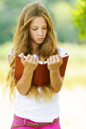 Beautiful teenage girl reading red book, against green of summer park. Beautiful teenage girl reading red book, against green of summer park.