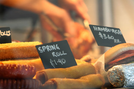 Inside a take away food store. Various hot food is on display and a person carving a chicken in the...
