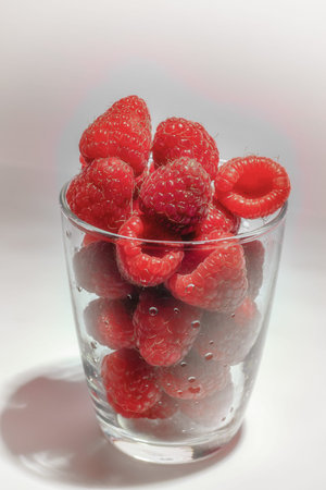 ripe raspberries in th glass on white table