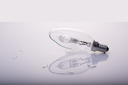 Closeup broken light bulb with reflection and glass pieces next to it,