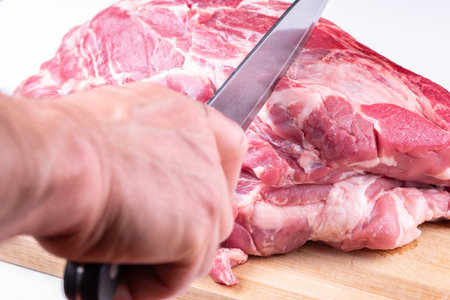 Butchers hand with knife cuts into a large piece of pork neck .