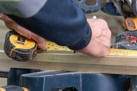 Carpenter using measure tape and marker on woodwork project.