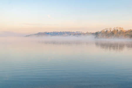 Cold foggy morning at the lake with reflections of trees .の写真素材