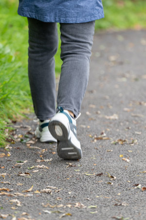 Legs of a young man walking along an asphalt path covered with fallen leavesの写真素材