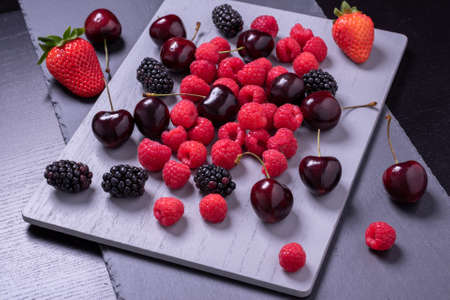 Cherries, raspberries and blackberries on grey stone board.の写真素材