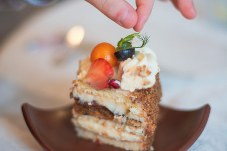 Fingers are reaching for peace of cake on brown plate
