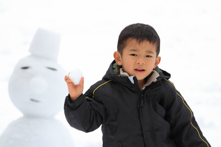 Japanese boy having snowball fight and snowmanの写真素材