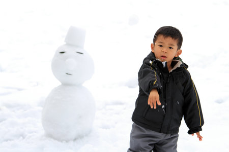 Japanese boy having snowball fight and snowmanの写真素材