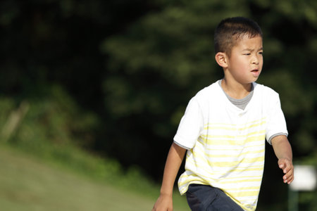Japanese boy running on the grass (second grade at elementary school)の写真素材