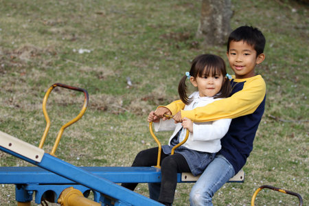 Japanese brother and sister on the seesaw (8 years old boy and 3 years old girl)の写真素材
