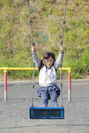 Japanese girl standing on the swing (5 years old)の写真素材