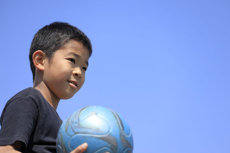 Japanese boy holding soccer ball under the blue sky (fifth grade at elementary school)の写真素材
