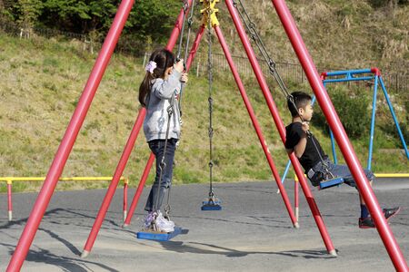 Japanese brother and sister on the swing  (10 years old boy and 5 years old girl)の写真素材