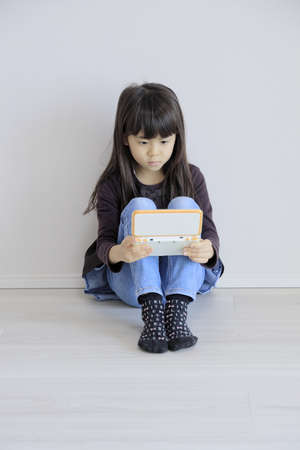 Japanese girl playing with video game console on the floor (7 years old)の素材 [FY310185581030]