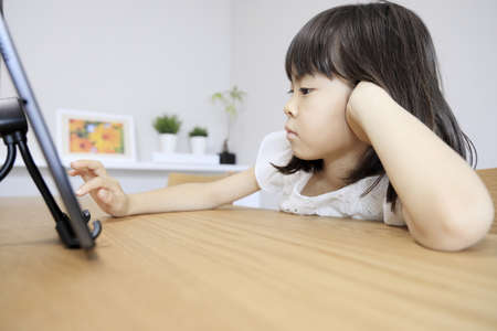 Japanese girl using a tablet PC in dining room (7 years old)の写真素材
