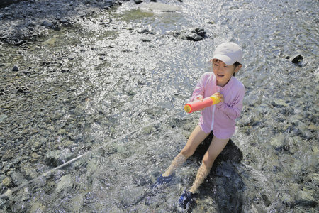 Japanese student girl playing in the river with water gun (7 years old)の写真素材