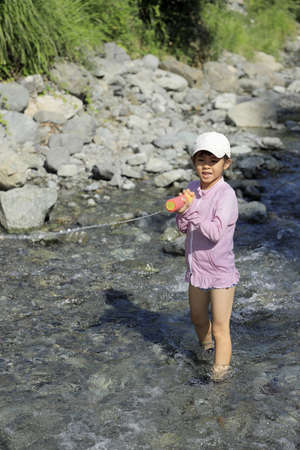 Japanese student girl playing in the river with water gun (7 years old)の写真素材