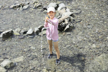 Japanese student girl playing in the river with water gun (7 years old)の写真素材