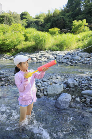 Japanese student girl playing in the river with water gun (7 years old)の写真素材