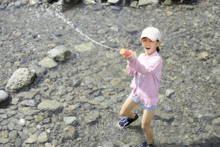 Japanese student girl playing in the river with water gun (7 years old)の写真素材