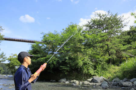 Japanese junior high school student playing in the river with water gun (12 years old boy)の写真素材