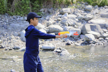 Japanese junior high school student playing in the river with water gun (12 years old boy)の写真素材